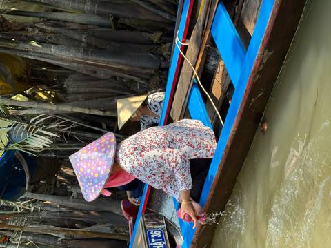 Two people in a boat wearing traditional hats navigating through mangroves.