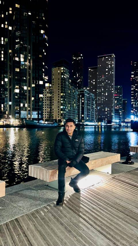 Person sitting by water with city lights behind.