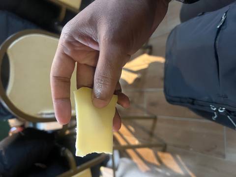 Close-up of a hand holding a piece of cheese indoors.