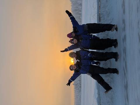       Group of friends enjoying a snowy landscape at sunset, posing with arms raised.
  