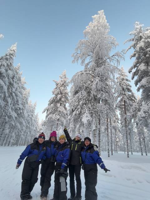       Group of friends posing in a snowy forest, wearing winter clothes and smiling.
  