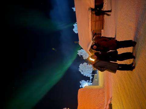 Three people standing with the northern lights and snow-covered landscape in the background.