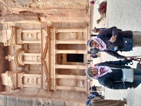 Two people in scarves and jackets posing in front of ancient Petra's Treasury.
