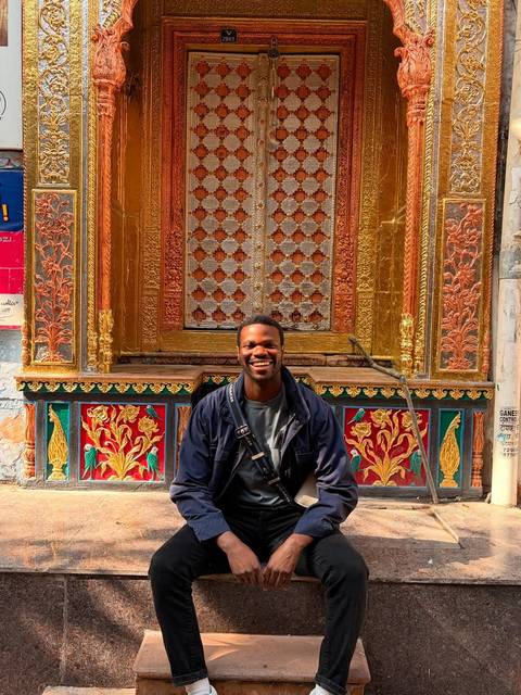       Person sitting in front of an ornate decorated wall.
  