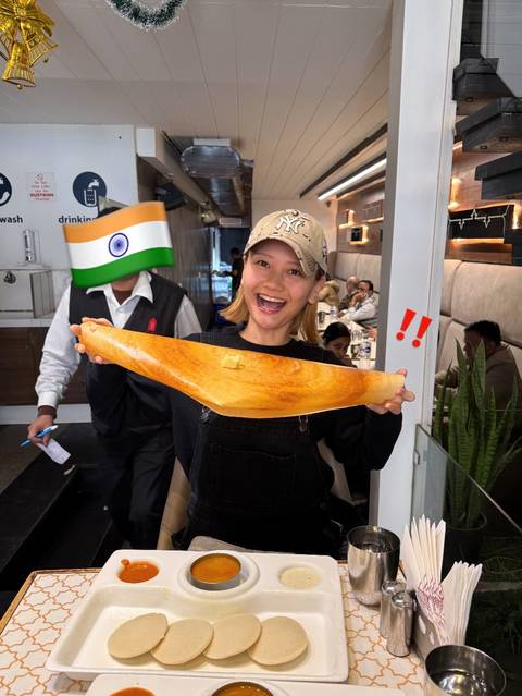       Person in a restaurant holding a large dosa with excitement.
  
