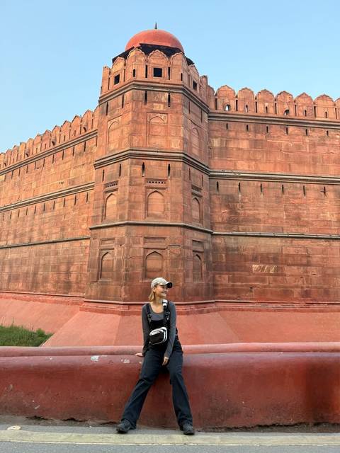       Person standing in front of a large red fort with intricate designs.
  
