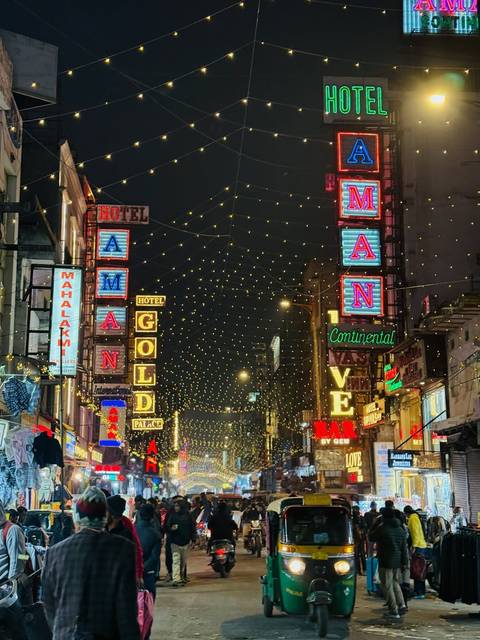       Night scene with neon signs and string lights on a busy street.
  