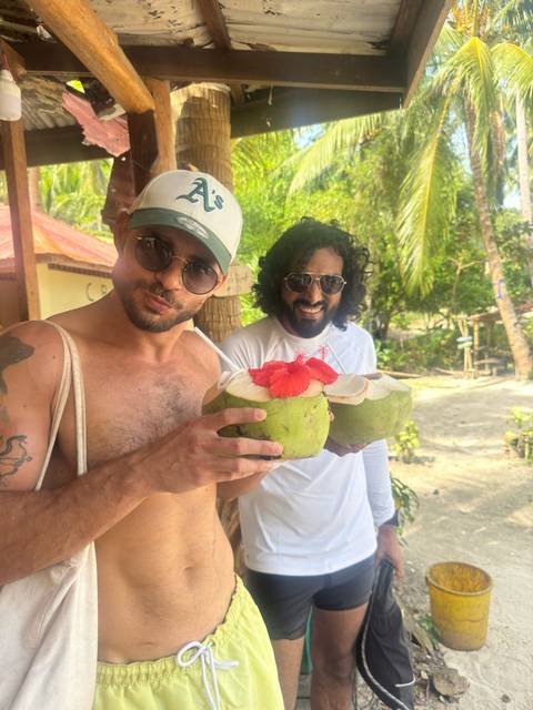 Two men holding coconuts with hibiscus flowers in a tropical setting