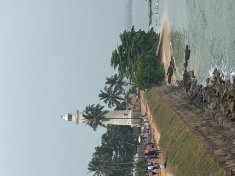       Lighthouse and coastline with people walking.
  