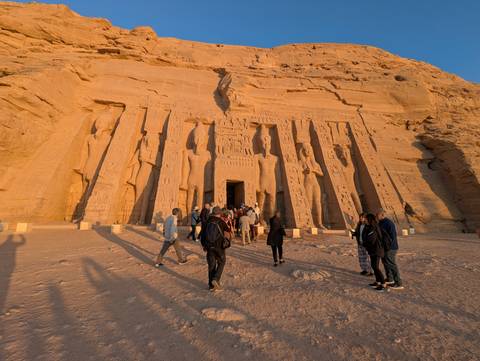 Facade of a temple with tall statues and people.