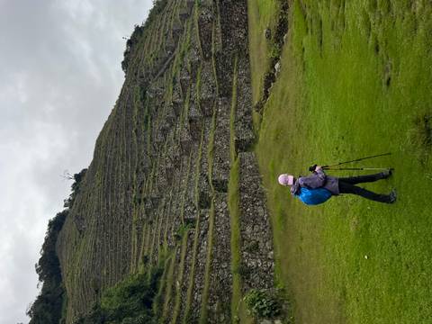       Person hiking near stone terraces on a hillside.
  