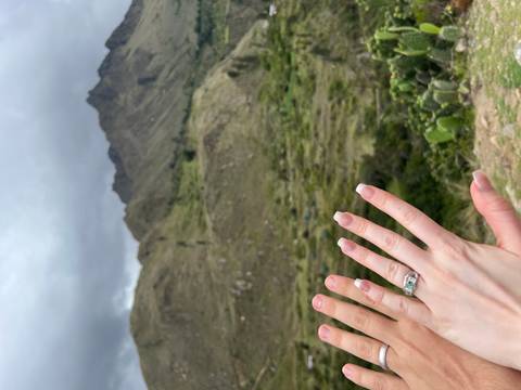       Close-up of hands with a ring, with mountains in the background.
  