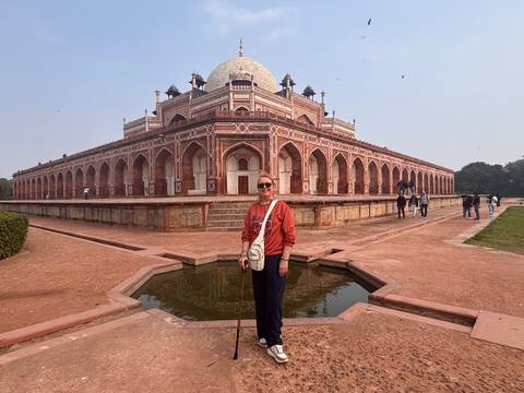       Visitor posing in front of a large historical mausoleum with intricate red stone architecture.
  