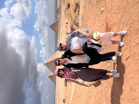       Three people posing near pyramids with cloudy sky in the background.
  