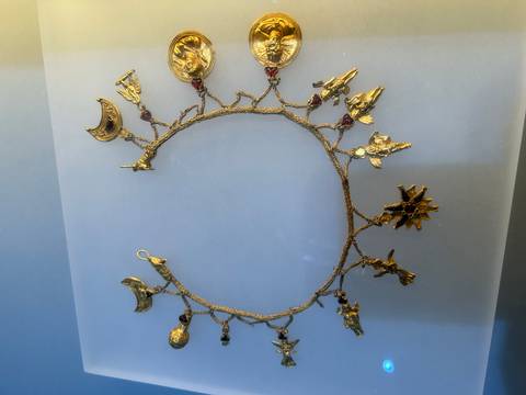       Golden necklace with intricate designs displayed in a museum.
  