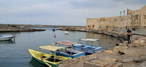       Colorful boats in a harbor next to an ancient stone fort.
  
