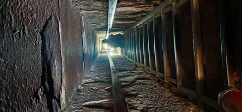       Narrow passage inside a pyramid with a person climbing.
  
