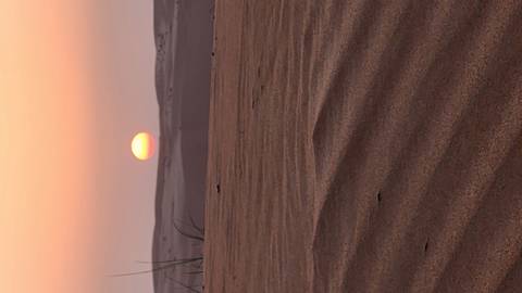       Desert dunes at sunset with a sun in the sky.
  