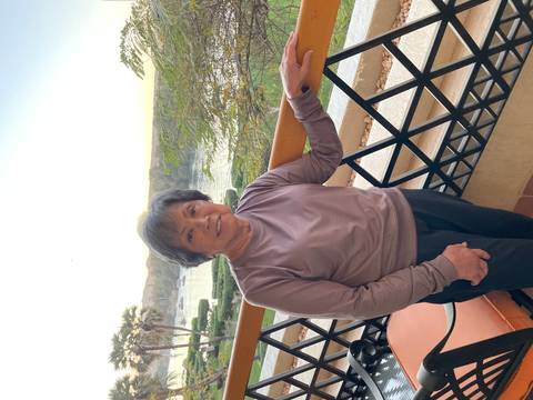 Portrait of an older woman on a balcony overlooking greenery.