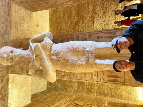       People posing with ancient statue inside a temple.
  