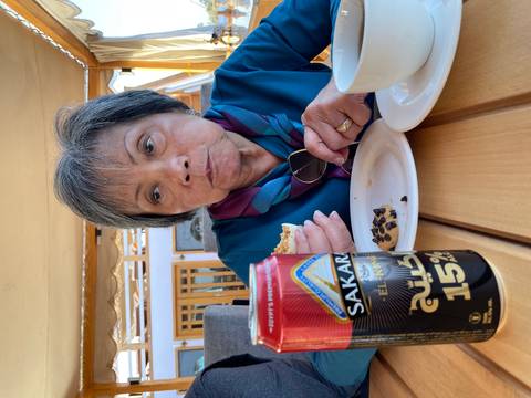 Older woman eating a snack with tea, can with Arabic text.