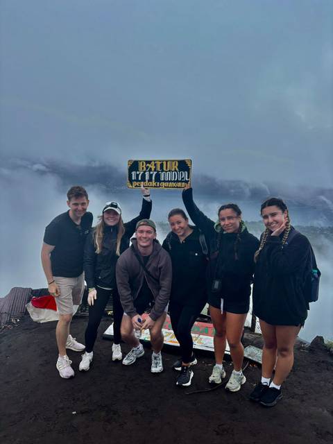 Group of friends holding a sign at a summit with foggy background.