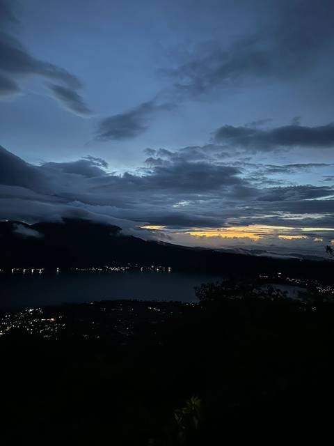 Landscape view of a lake with mountains and cloudy sky during sunset.