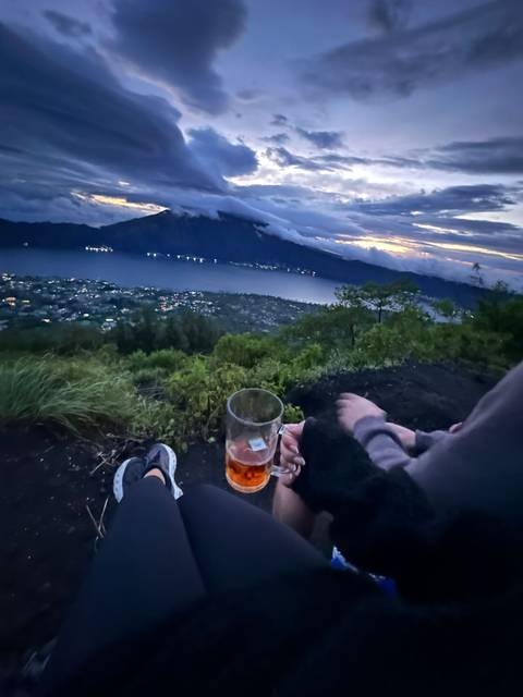 View from a mountain with a lake, focusing on someone holding a drink.