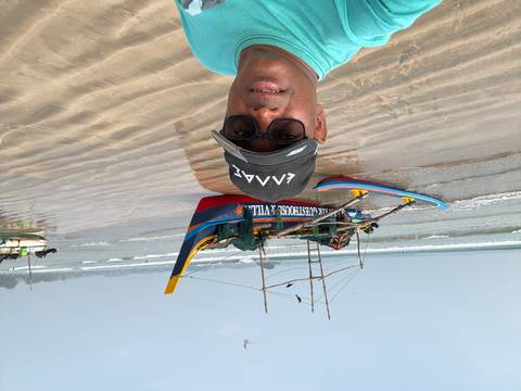       A person taking a selfie on a beach with a fishing boat.
  