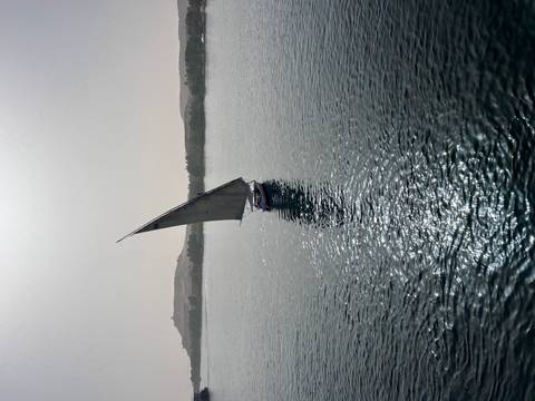 Traditional sailboat on expansive water with distant hills.