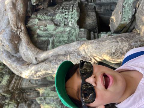 Young person taking a selfie with a tree-covered temple in the background.