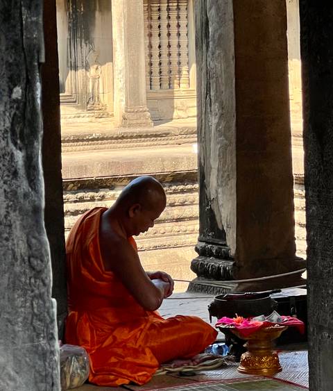 Monk in orange robe sitting in contemplation inside ancient temple ruins.