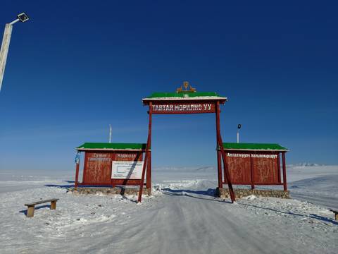 Entrance sign to a snowy landscape with a clear blue sky.