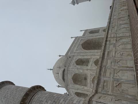       Marble façade and large dome of the Taj Mahal rising against a hazy sky
  