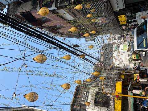       Urban street with a canopy of decorative gourds and tangled overhead wiring against blue sky.
  