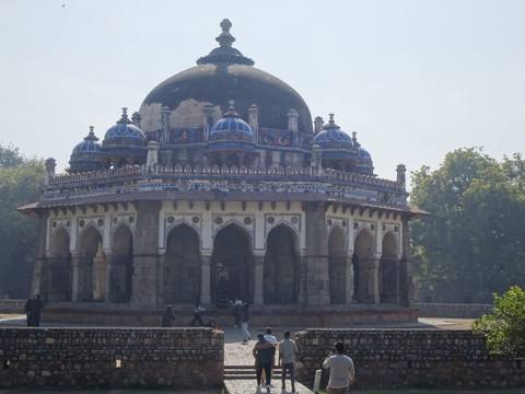       Domed tomb with blue tile accents surrounded by trees in a Mughal garden setting.
  