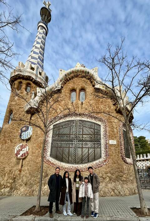       Whimsical Gaudí gatehouse with mosaic decorations and bare tree branches in Park Güell, Barcelona.
  