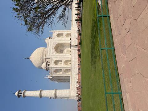       Side perspective of the Taj Mahal rising above manicured lawns against a clear blue sky.
  