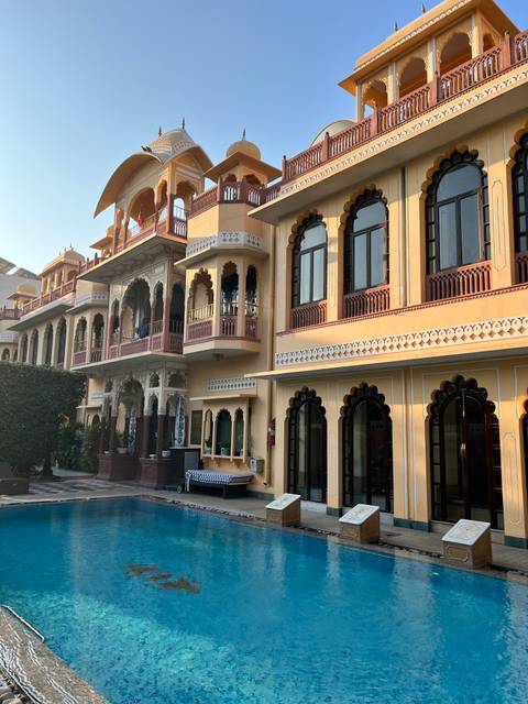       Facade of a heritage palace hotel in Jaipur with intricate arched windows and pastel colors lit by morning sun
  