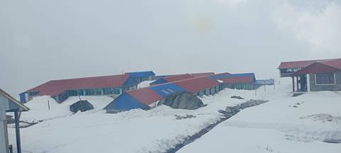       Snow-covered lodges and pathways at Annapurna Base Camp beneath a cloudy sky.
  
