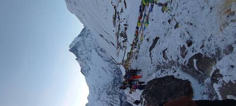       Trekkers approach a string of colourful prayer flags with Machhapuchhare towering behind.
  
