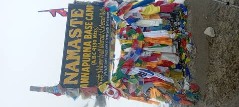       Decorated welcome sign for Annapurna Base Camp draped in colourful prayer flags against a snowy backdrop.
  
