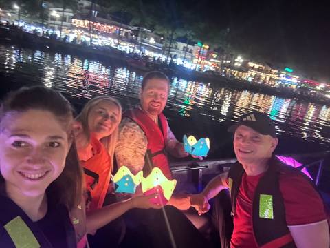       Travellers hold paper lanterns while floating on a riverboat amid the colourful night lights of Hội An.
  