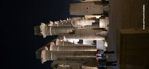       Massive columns and statues of Luxor Temple illuminated at night with visitors exploring the courtyard.
  