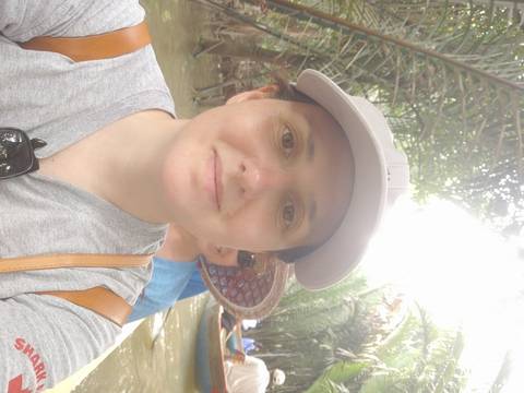       Selfie of a traveller in a cap on a small jungle river boat with another person partially visible behind.
  