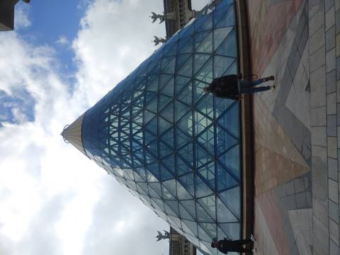       Traveller approaching a modern glass-pyramid structure under a partly cloudy sky.
  