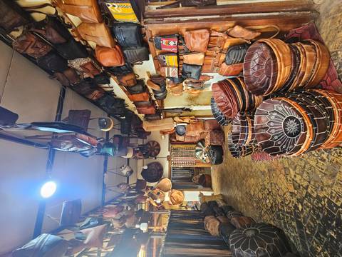       Interior of a Moroccan leather goods shop with baskets and bags hanging from the ceiling.
  