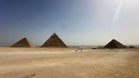       Wide desert panorama of the three main pyramids of Giza beneath a hazy blue-grey sky.
  