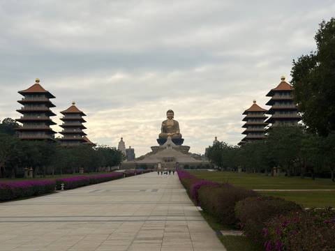       Grand avenue leading to the giant seated Buddha at Fo Guang Shan flanked by pagodas and purple flowers.
  