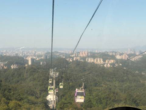       Blurred view through gondola glass of Taipei city and forested hills below suspension cables.
  